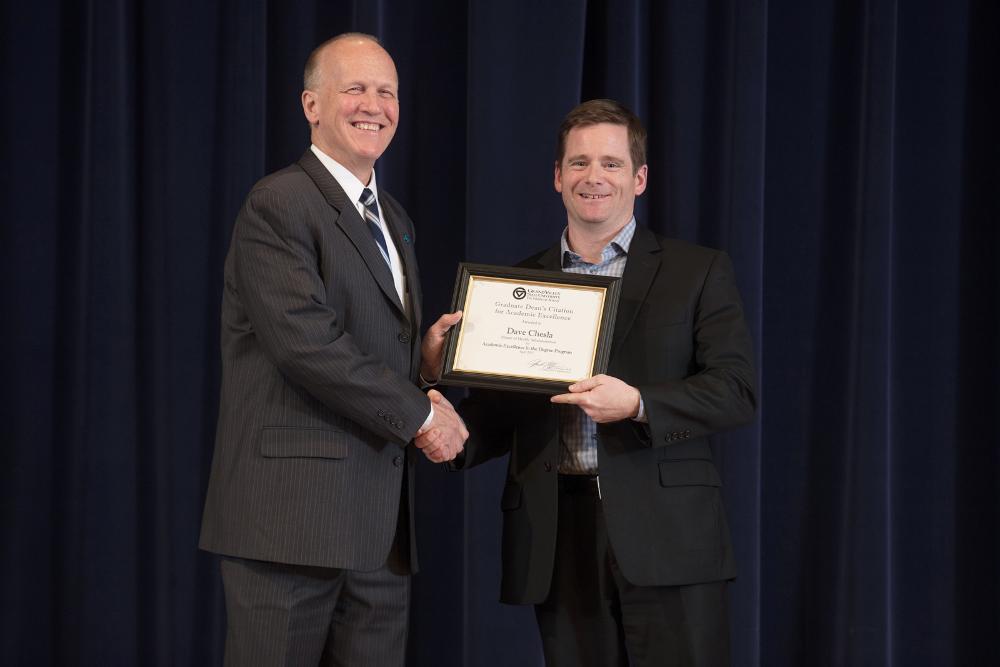 Doctor Potteiger posing for a photo with an award recipient in a black suit and blue striped shirt